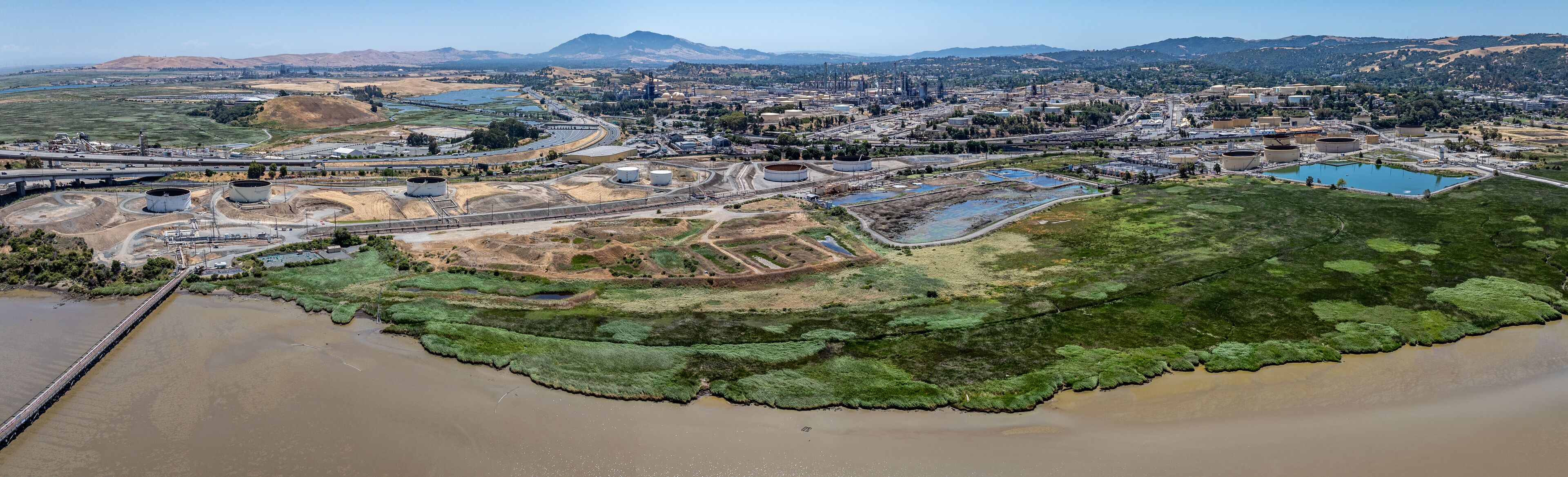 An aerial view of an industrial area with storage tanks, a bridge, and a river.