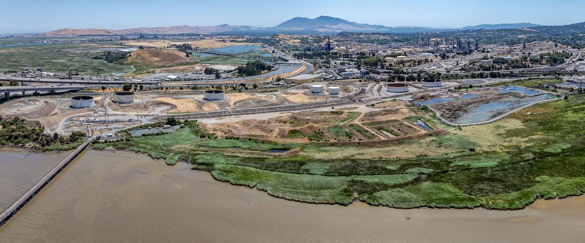 An aerial view of an industrial area with storage tanks, a bridge, and a river.
