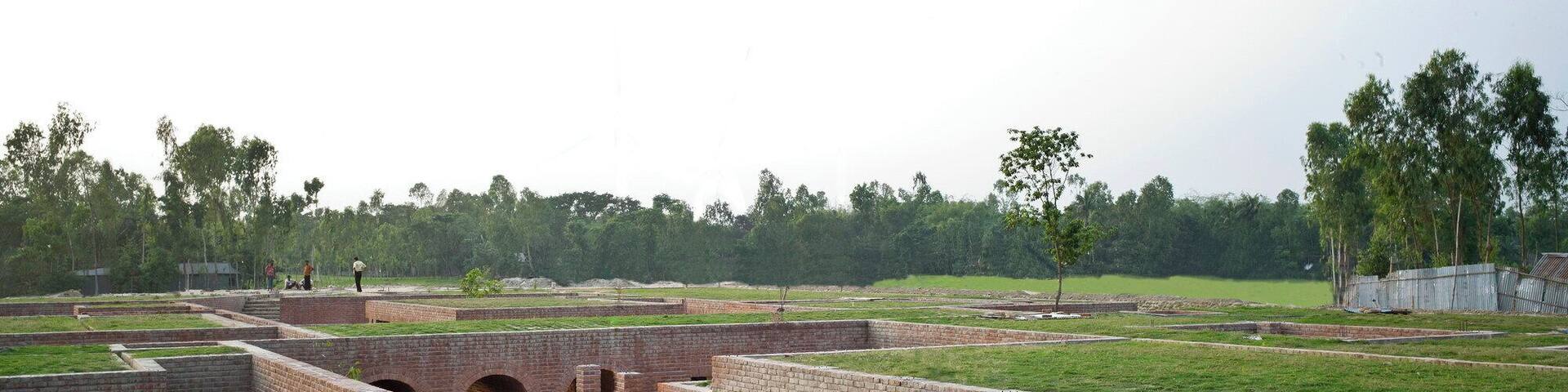 A rural training centre inspired by one of the country’s oldest urban archaeological sites.
The Centre was created to train staff of an NGO working with people inhabiting nearby chars, or riverine islands. Offices, a library, meeting rooms, and prayer and tea rooms are included in pavilion-like buildings surrounded by courts and pools. The Centre is also rented out for meetings, training, and conferences for income generation. The local hand-made brick construction has been inspired by the monastic aesthetic of the 3rd century BC ruins of Mahasthangahr, the earliest urban archaeological site yet found in Bangladesh. Structural elements are of reinforced concrete and finishes also include timber and stone. The naturally ventilated structures have green roofs. The Centre is located in an agricultural area susceptible to flooding and earthquakes, and whose low-bearing soil has a low bearing capacity. As a result, an embankment has been constructed with a water run-off pumping facility. Constructed and finished primarily of one material - local hand-made bricks - the spaces are woven out of pavilions, courtyards, pools and greens, corridors and shadows. The Friendship Centre is divided into two sections, the outer Ka block for the offices, library and training classrooms and the inner Kha block for the residential section. At a time, 80 people can be trained here in four separate classrooms. Simplicity is the intent, monastic is the feel.
Award Cycle: 2014-2016 Cycle http://www.akdn.org/award-cycle/2016-cycle