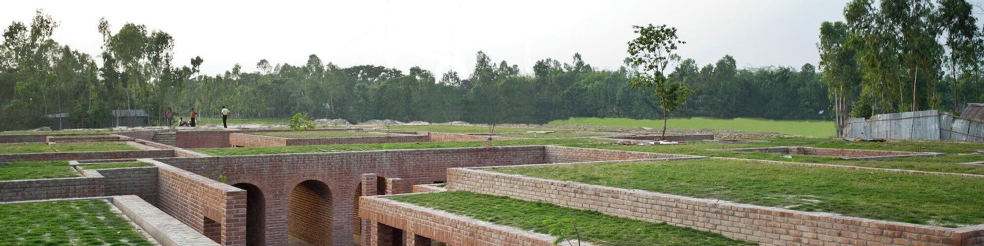 A rural training centre inspired by one of the country’s oldest urban archaeological sites.
The Centre was created to train staff of an NGO working with people inhabiting nearby chars, or riverine islands. Offices, a library, meeting rooms, and prayer and tea rooms are included in pavilion-like buildings surrounded by courts and pools. The Centre is also rented out for meetings, training, and conferences for income generation. The local hand-made brick construction has been inspired by the monastic aesthetic of the 3rd century BC ruins of Mahasthangahr, the earliest urban archaeological site yet found in Bangladesh. Structural elements are of reinforced concrete and finishes also include timber and stone. The naturally ventilated structures have green roofs. The Centre is located in an agricultural area susceptible to flooding and earthquakes, and whose low-bearing soil has a low bearing capacity. As a result, an embankment has been constructed with a water run-off pumping facility. Constructed and finished primarily of one material - local hand-made bricks - the spaces are woven out of pavilions, courtyards, pools and greens, corridors and shadows. The Friendship Centre is divided into two sections, the outer Ka block for the offices, library and training classrooms and the inner Kha block for the residential section. At a time, 80 people can be trained here in four separate classrooms. Simplicity is the intent, monastic is the feel.
Award Cycle: 2014-2016 Cycle http://www.akdn.org/award-cycle/2016-cycle