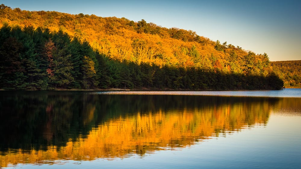 Un lac paisible qui reflète une colline boisée aux couleurs automnales.