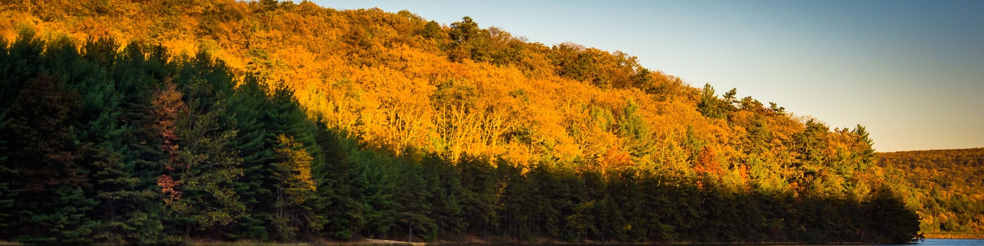 A calm lake reflecting a forested hillside with autumn foliage.