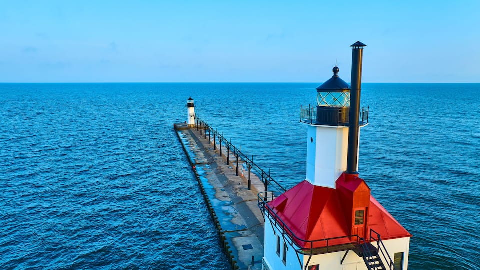 A lighthouse with a red roof and a white tower, extending into the blue sea.