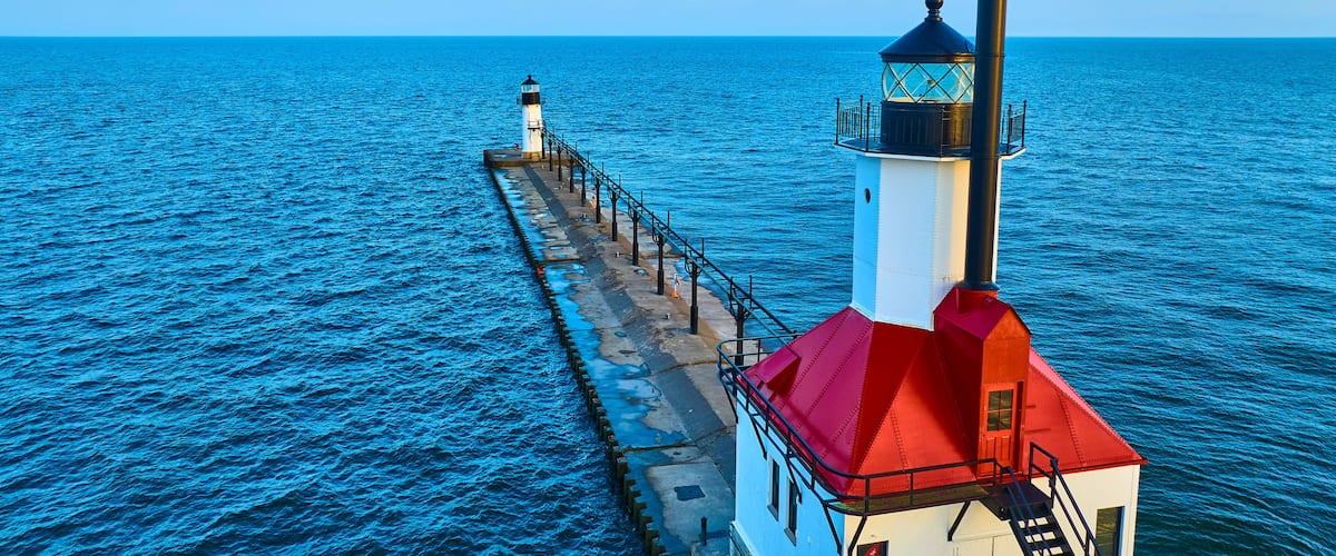A lighthouse with a red roof and a white tower, extending into the blue sea.