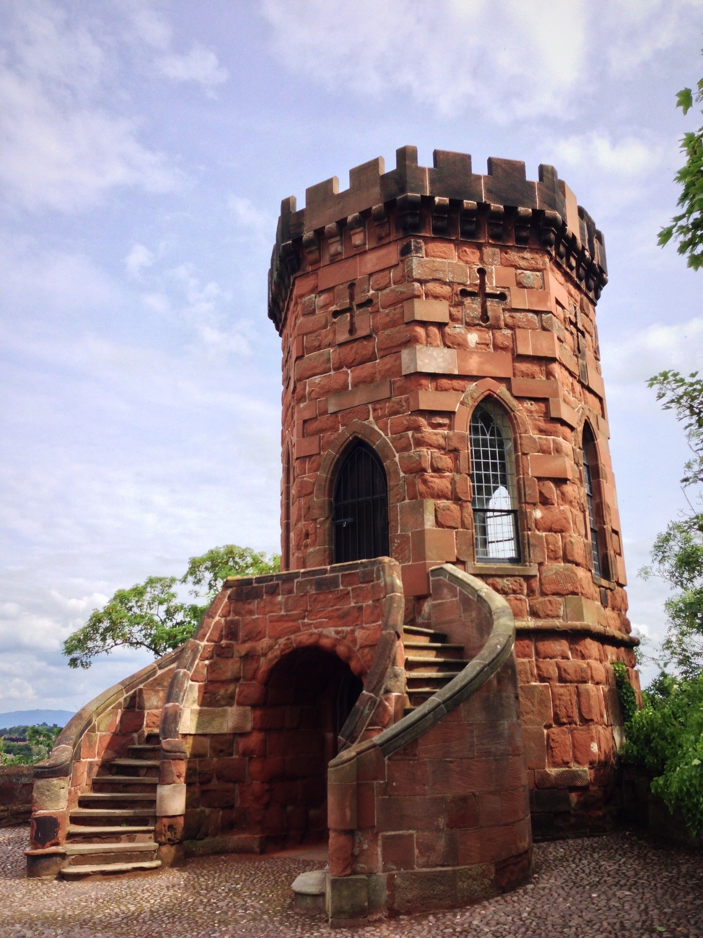 Una torre histórica con una escalera en espiral que lleva a una ventana, rodeada de follaje.