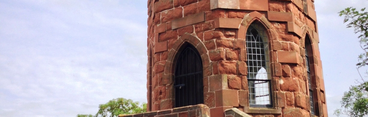 A historic tower with a spiral staircase leading to a window, surrounded by greenery.
