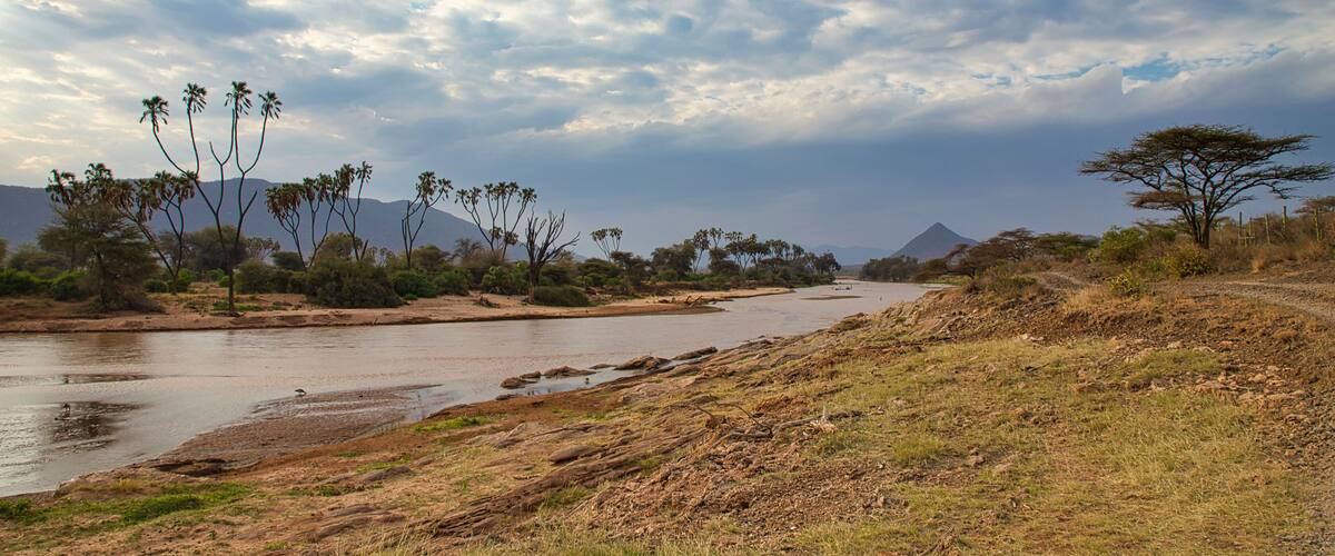 A river winding through a dry landscape with sparse vegetation and a prominent mountain in the background.
