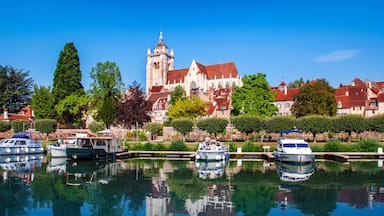 A historic building with a tower, a calm waterway with boats, and lush greenery.