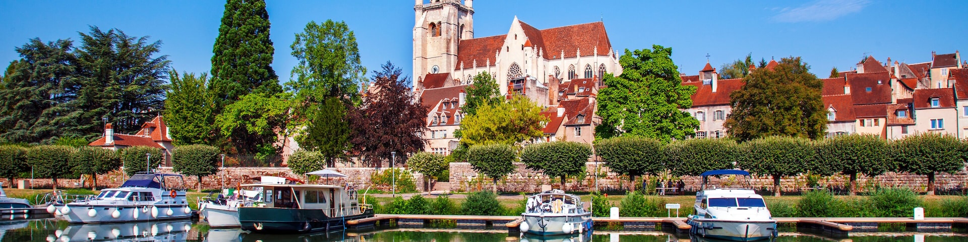 Un edificio histórico con una torre, una vía fluvial tranquila con barcos y abundante vegetación.