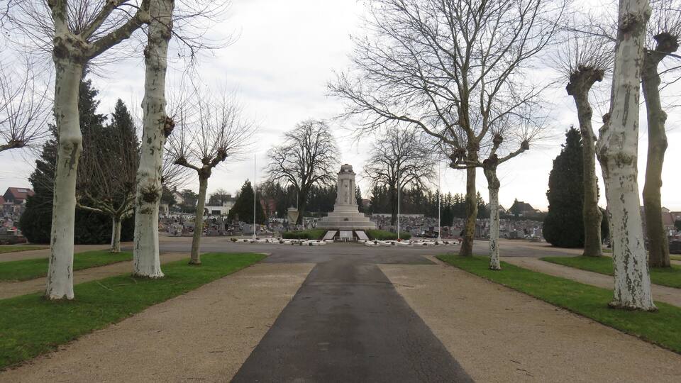 A park with a central monument, surrounded by trees and a pathway.