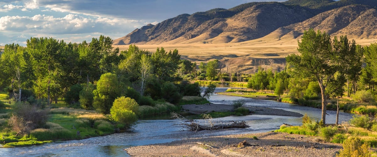 A river flowing through a valley with mountains in the background and a clear sky.