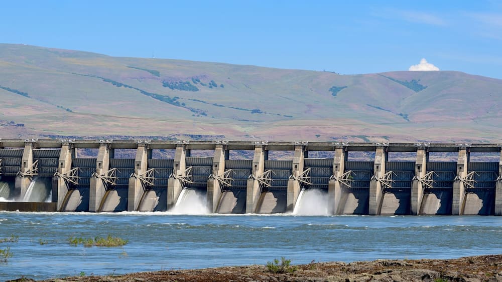 A dam with multiple spillways releasing water, surrounded by a mountainous landscape.