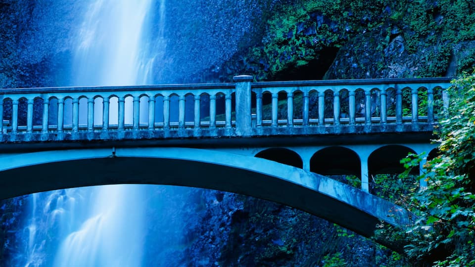 A stone bridge with arches spanning a waterfall.
