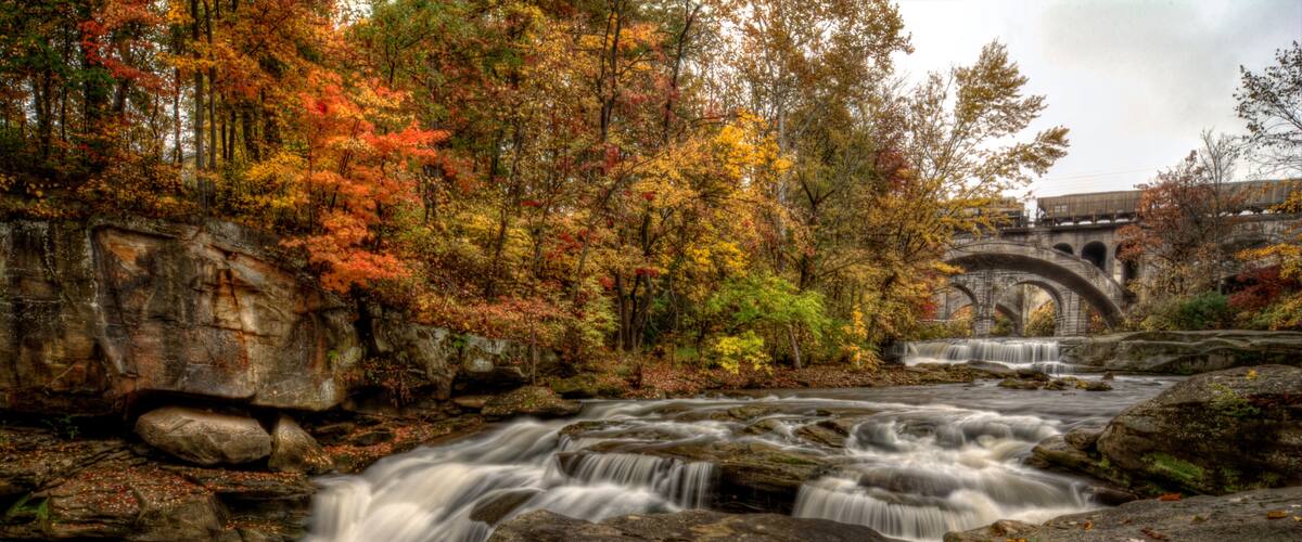 A waterfall flowing over rocks in a forest with autumn leaves.