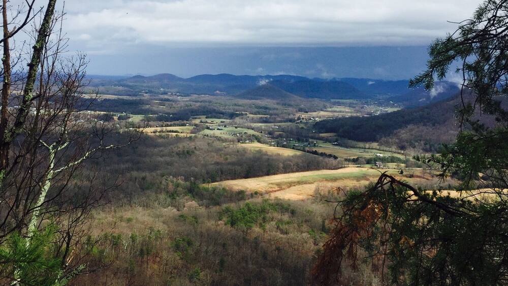 A mountainous landscape with a valley, forested areas, and a distant view of a town.