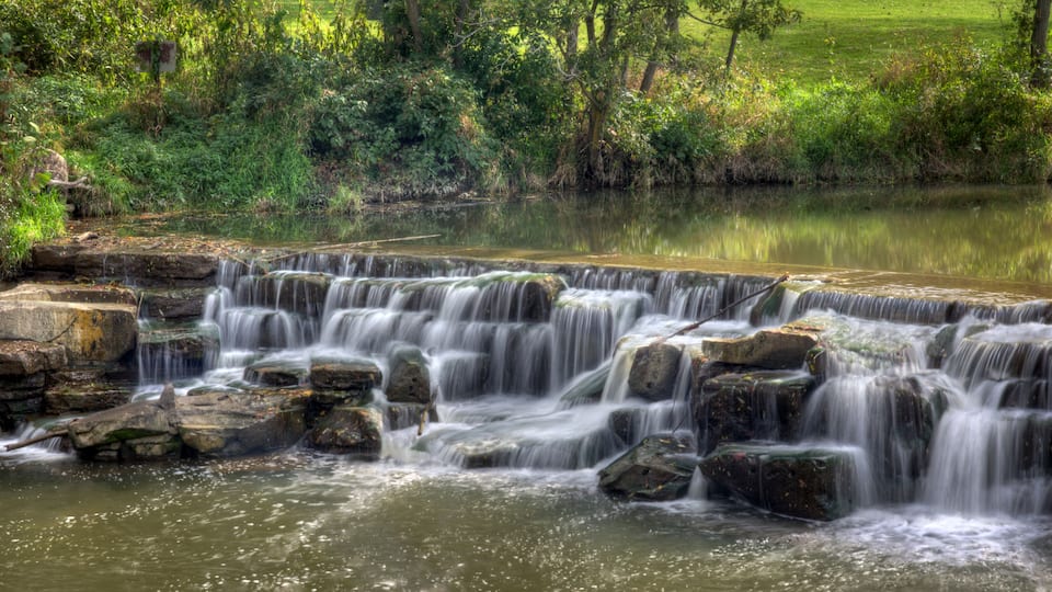 A multi-tiered waterfall cascading over rocks in a lush, green landscape.