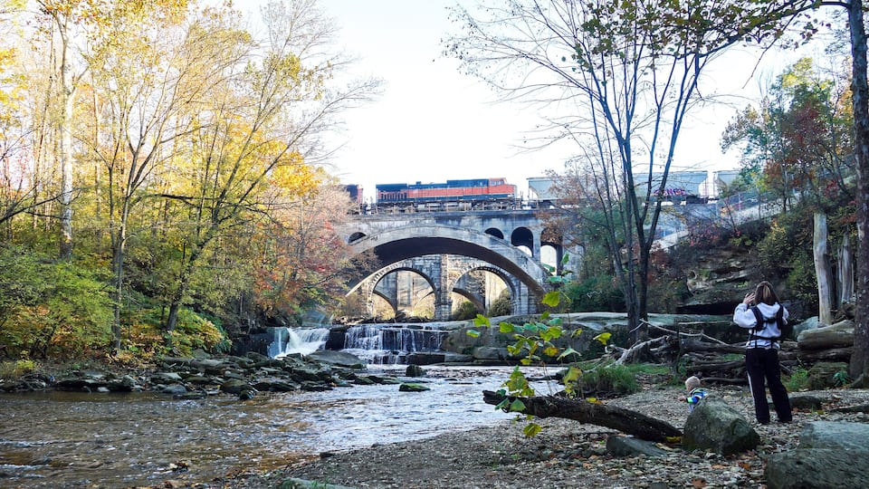 A river with a waterfall, a stone bridge, and autumn foliage.