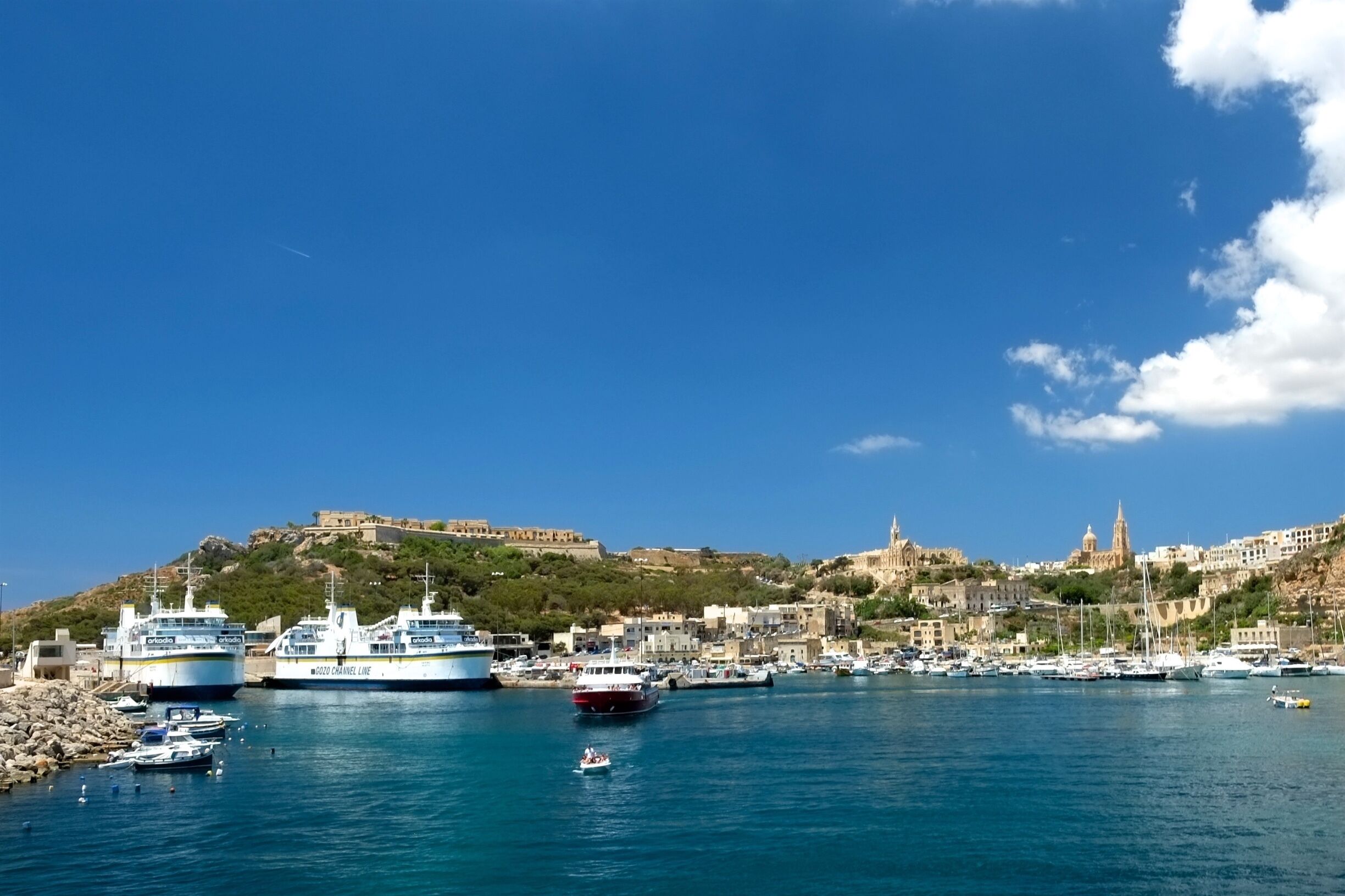 A coastal town with a historic fort on a hill, a harbor with boats, and a clear blue sky.