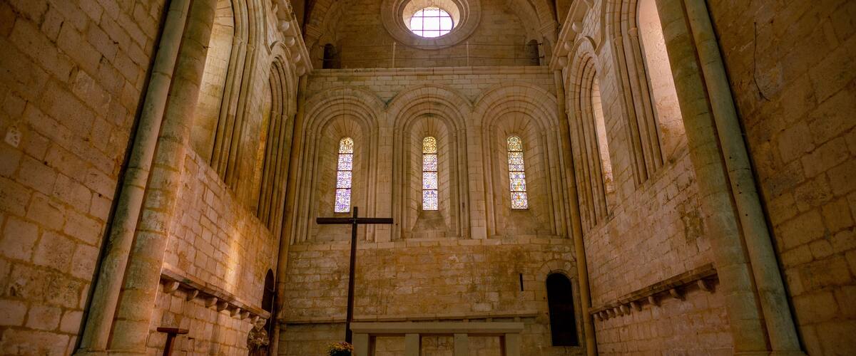 An interior of a cathedral with arched windows, a large cross, and a stone altar.
