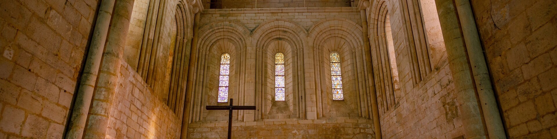 An interior of a cathedral with arched windows, a large cross, and a stone altar.
