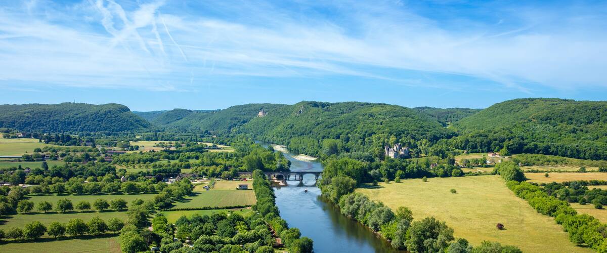 A river flowing through a valley with lush green hills and scattered buildings.