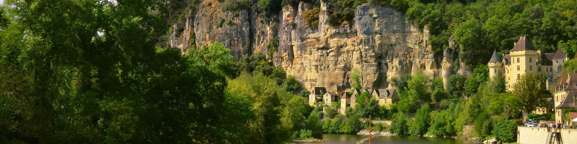 Un río con un barco, un castillo y un acantilado cubierto de bosque.