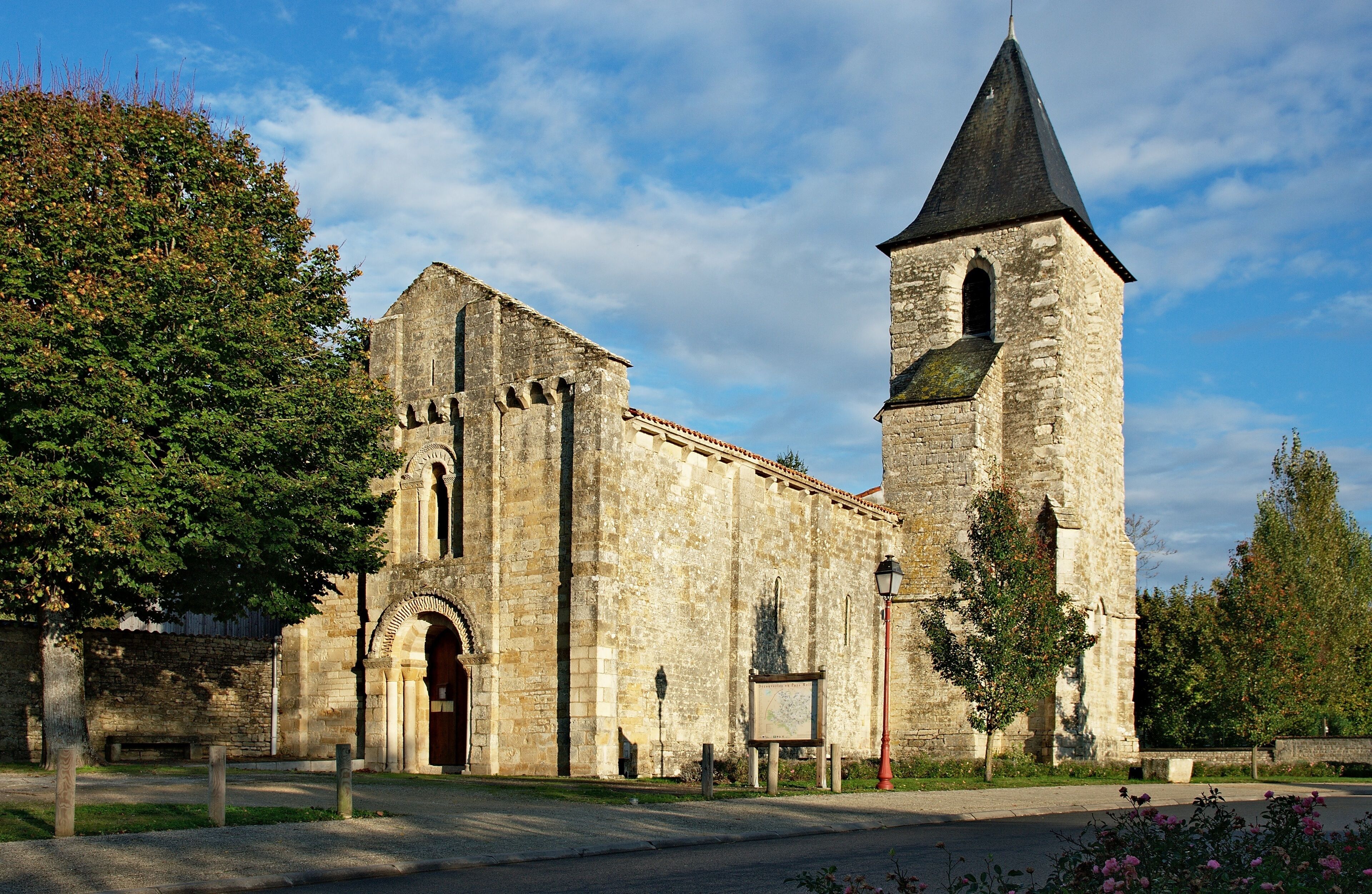 An old stone church with a bell tower and a large tree in front.