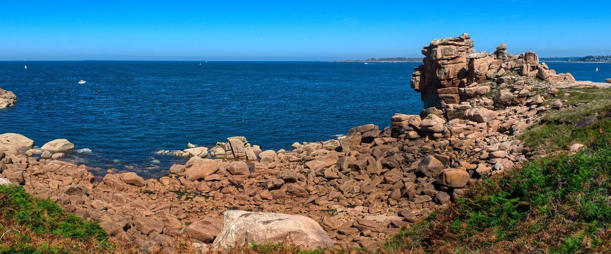 A rocky coastline with clear blue waters and a sailboat in the distance.