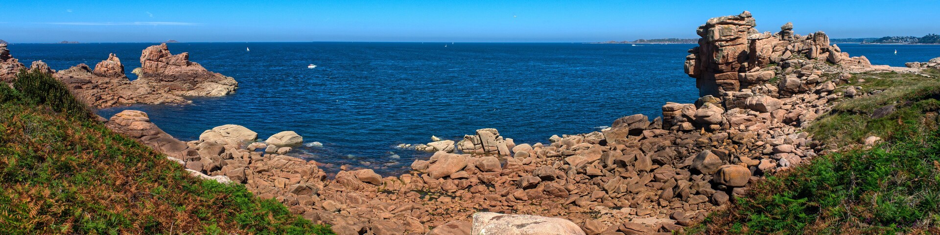 A rocky coastline with clear blue waters and a sailboat in the distance.
