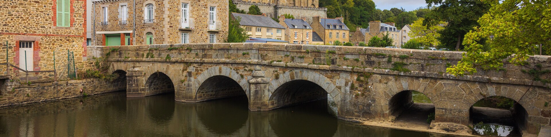 Un puente de piedra sobre un río tranquilo, con edificios históricos e iglesia al fondo.