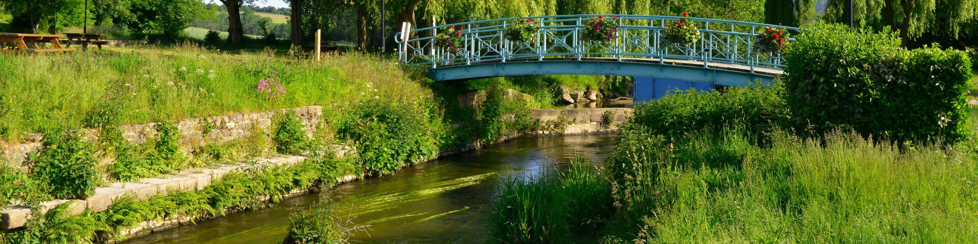 Panoramique La Loisance traversée par un pont fleuri, coule dans un parc de verdure à Antrain (35560 Val-Couesnon), département d'Île-et-Vilaine en région Bretagne, France