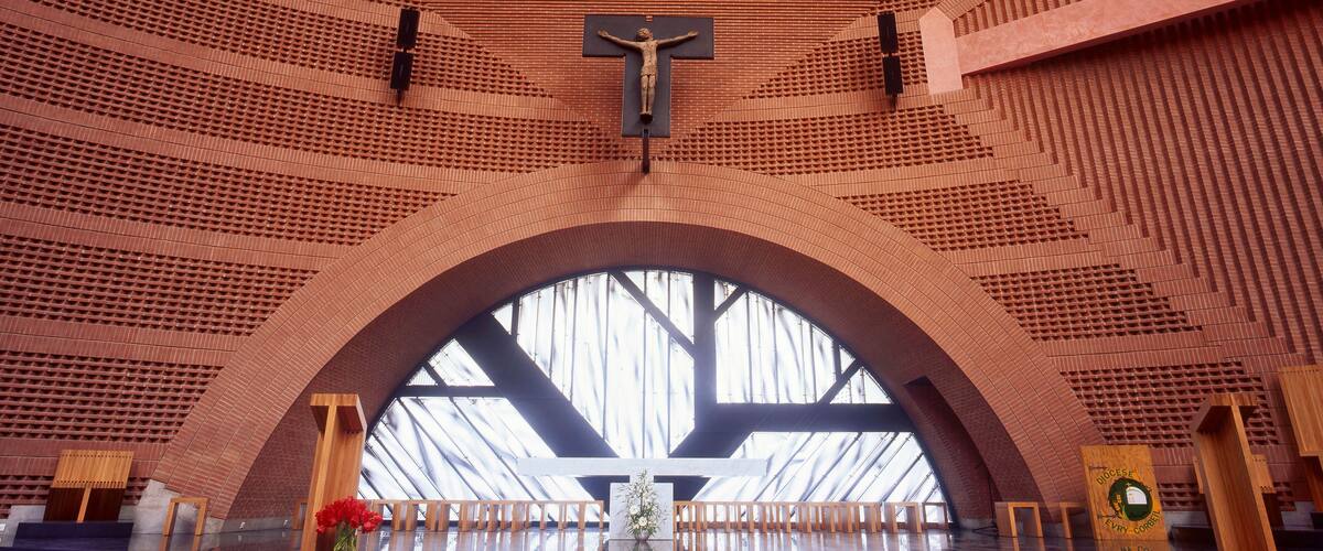A church interior with a crucifix, arched ceiling, and wooden pews.