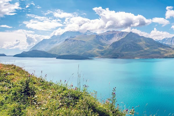 Un lac turquoise, entouré de collines verdoyantes et de montagnes, sous un ciel dégagé.