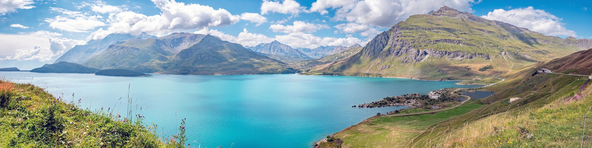 A turquoise lake surrounded by green hills and mountains under a clear sky.