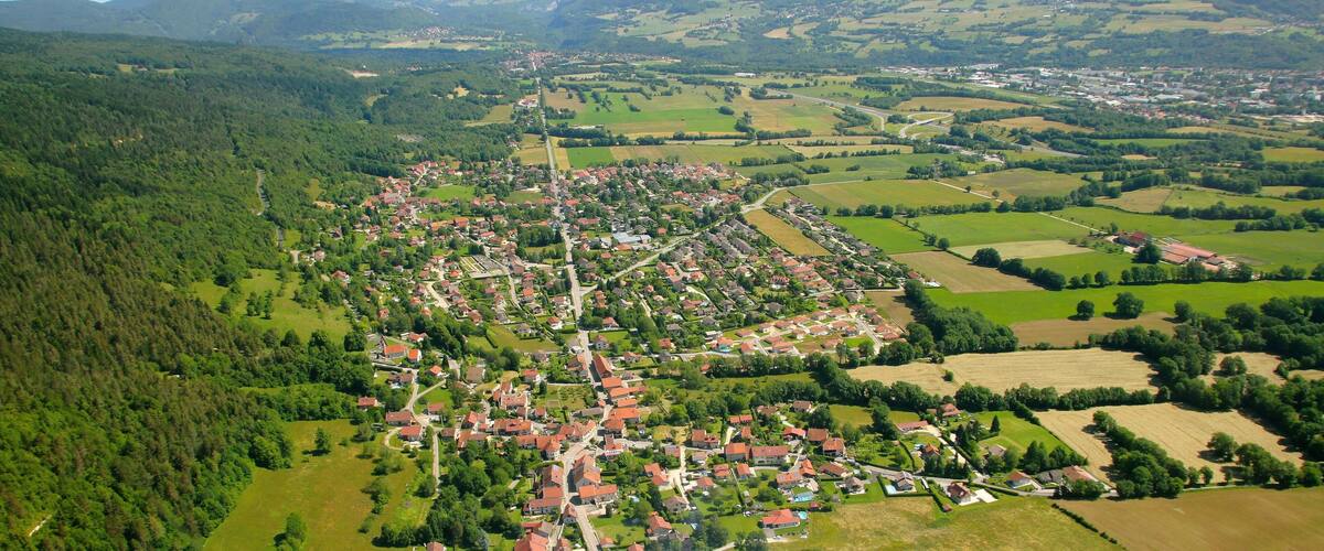 A mountainous landscape with a village nestled in the valley surrounded by fields and forests.