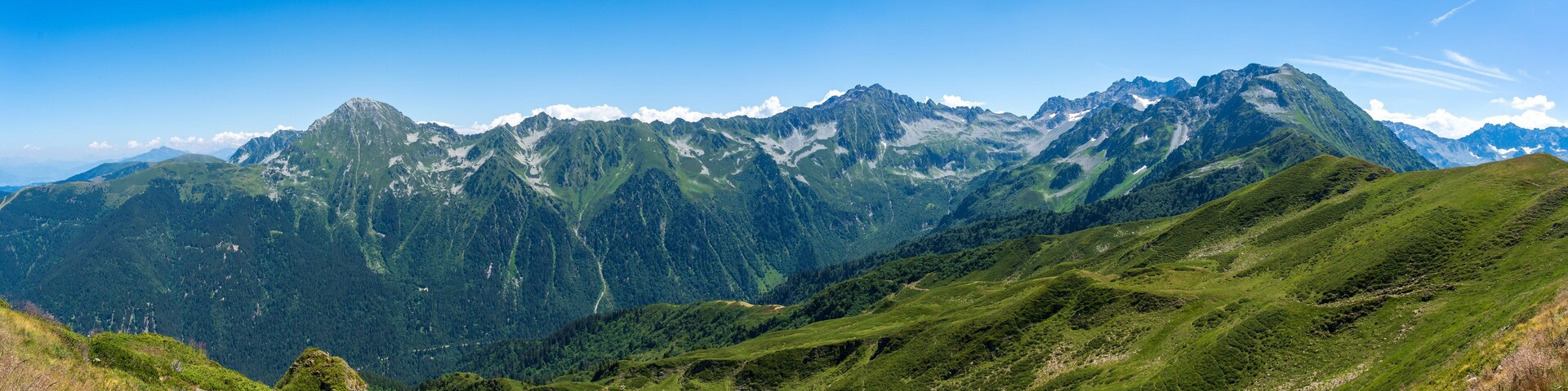 Cordillera con valles verdes y picos escarpados bajo un cielo azul despejado.