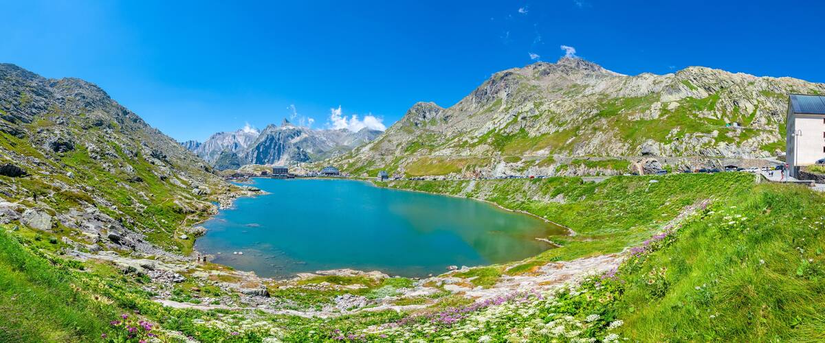A lake surrounded by mountains, a small building, and a clear blue sky.
