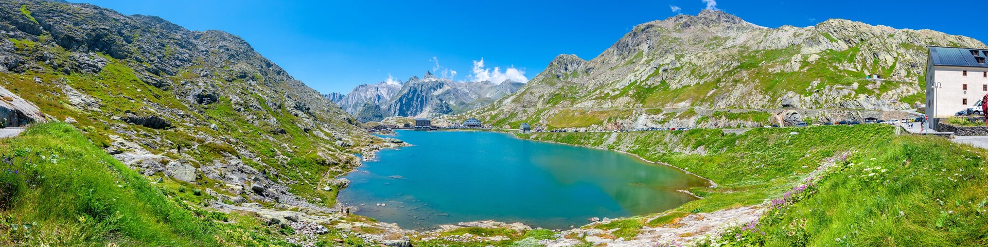 A lake surrounded by mountains, a small building, and a clear blue sky.