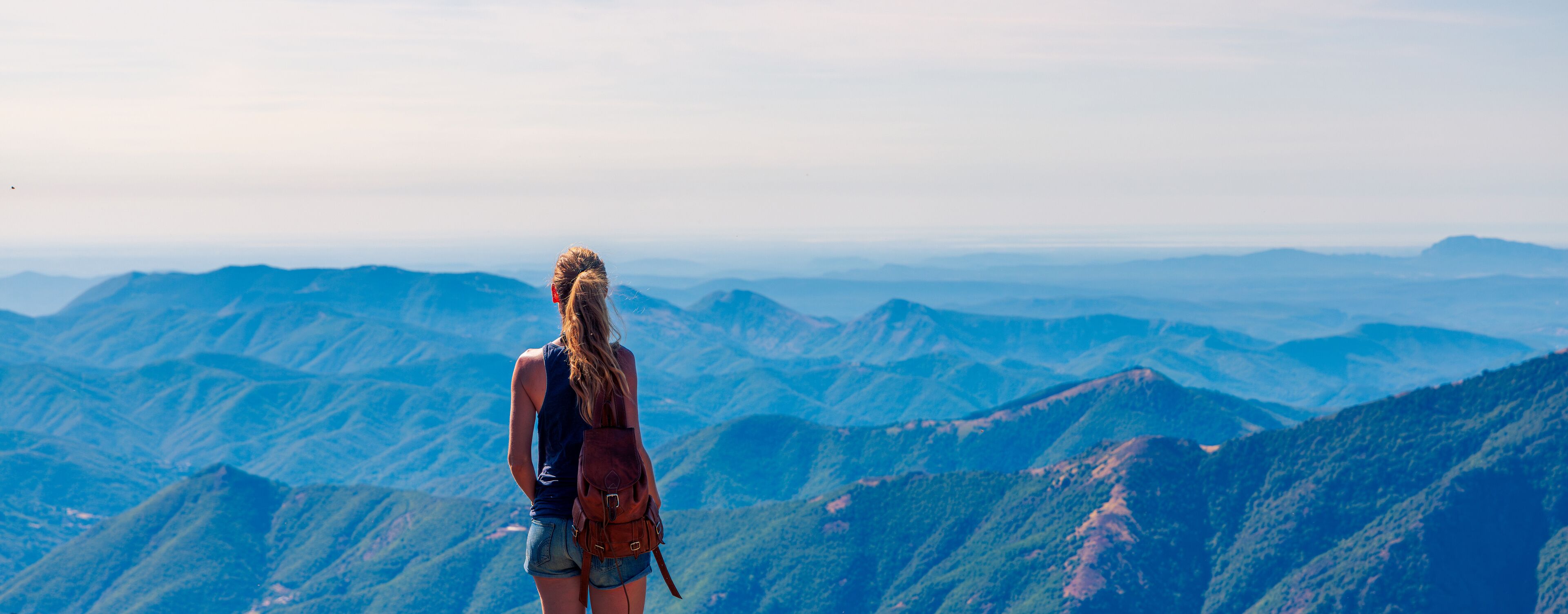 A person standing on a mountain ridge overlooking a vast mountainous landscape.