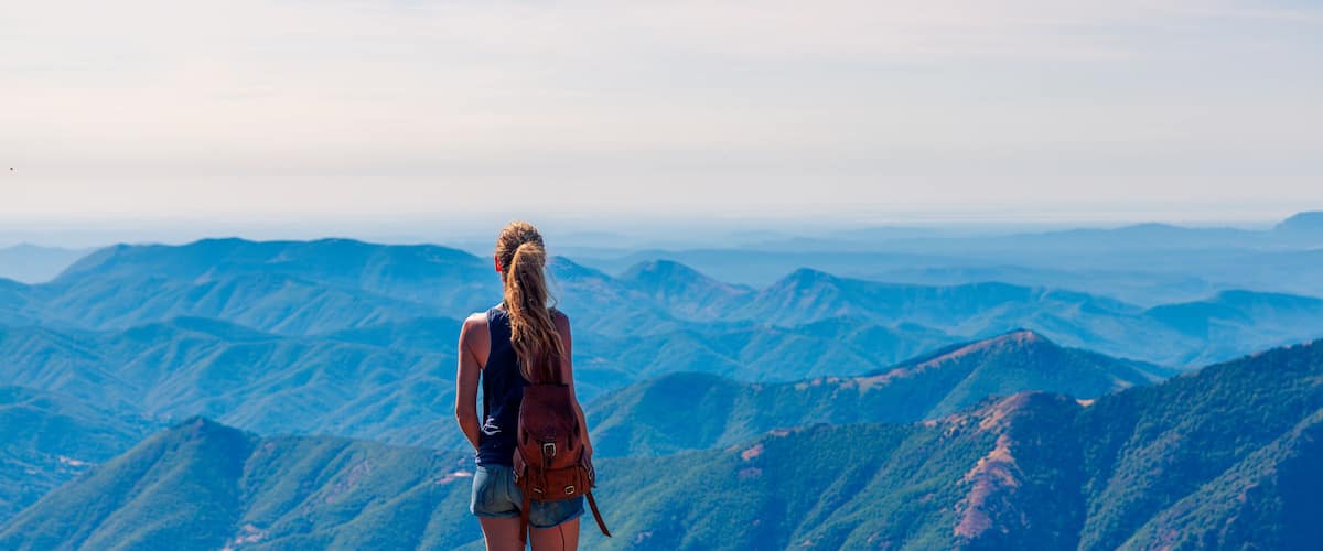 A person standing on a mountain ridge overlooking a vast mountainous landscape.
