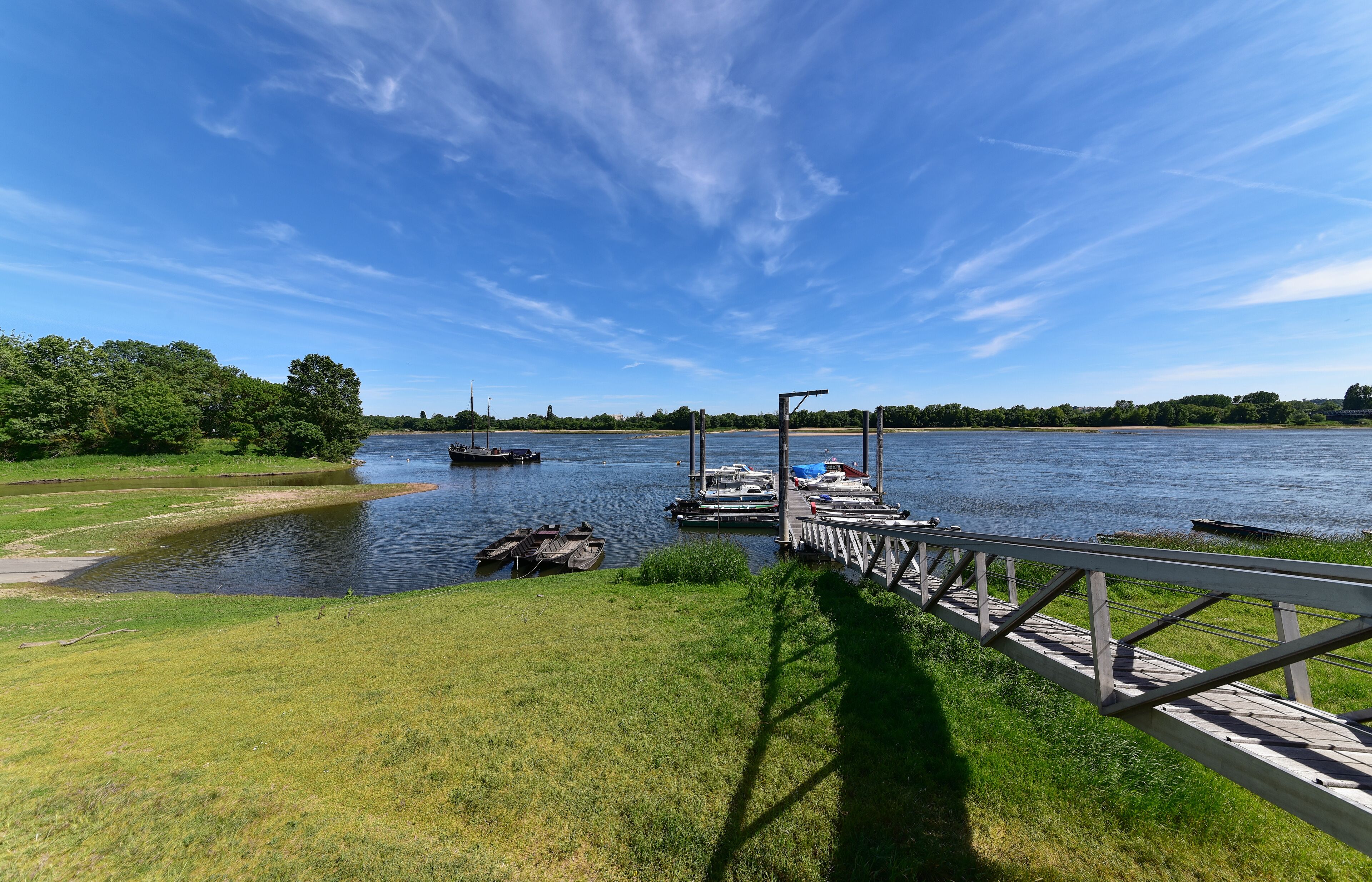 A river with boats docked at a pier, surrounded by greenery and a clear sky.