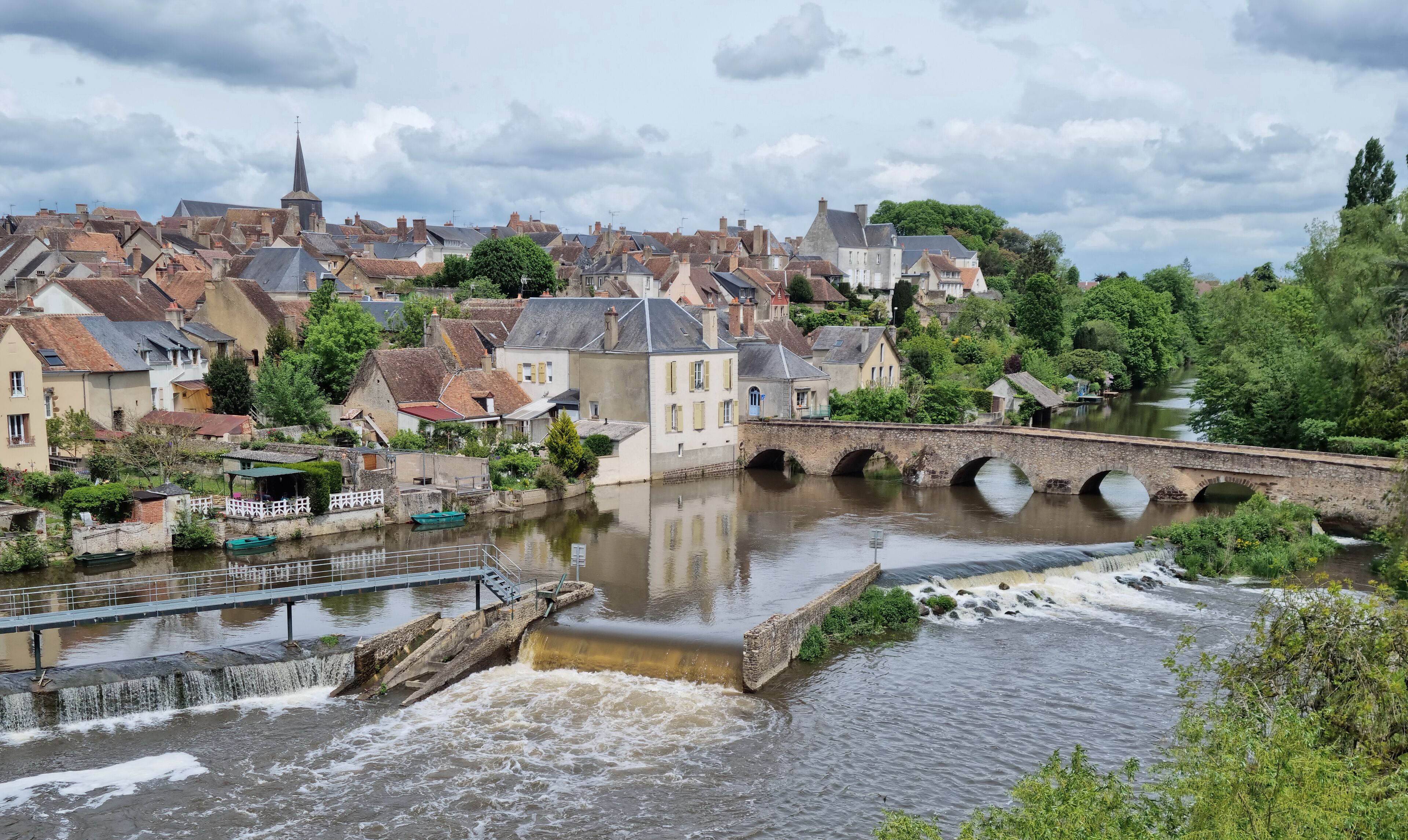 A river flowing under a stone bridge with houses on the opposite bank.