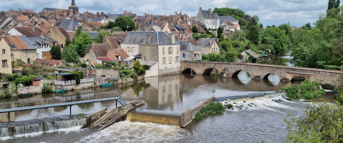 A river flowing under a stone bridge with houses on the opposite bank.