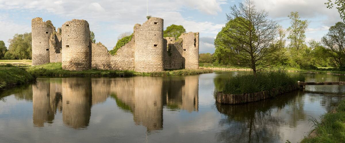 A historic stone castle with a moat and reflection in the water.