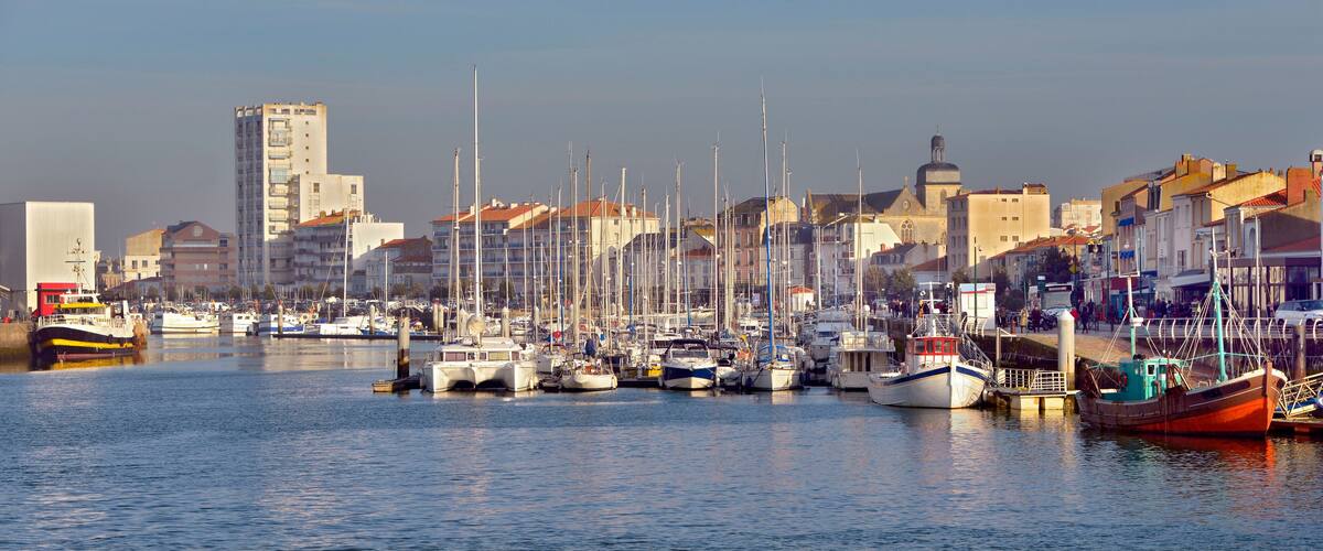 A marina with various boats docked, surrounded by buildings and a clear sky.