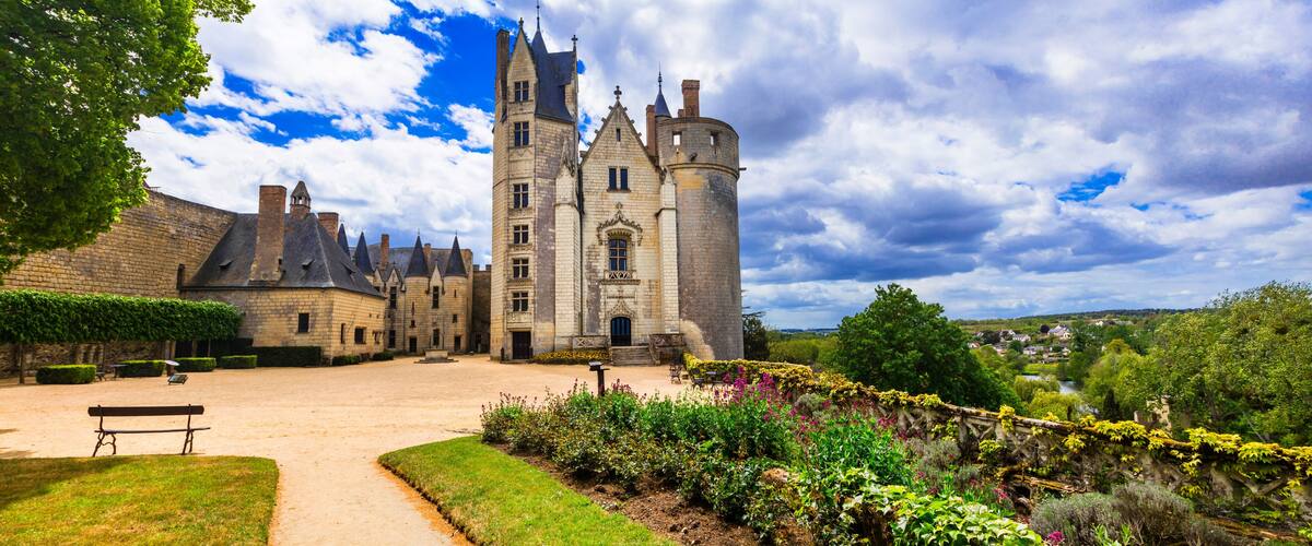 A historic castle with a large tower, surrounded by well-maintained gardens and a clear sky.
