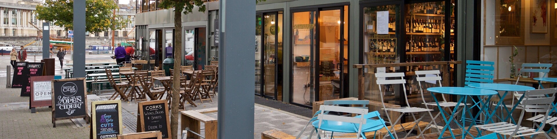 Un área de estar al aire libre con sillas de madera y azules, un cartel que enumera los platillos y un escaparate con puertas de cristal.