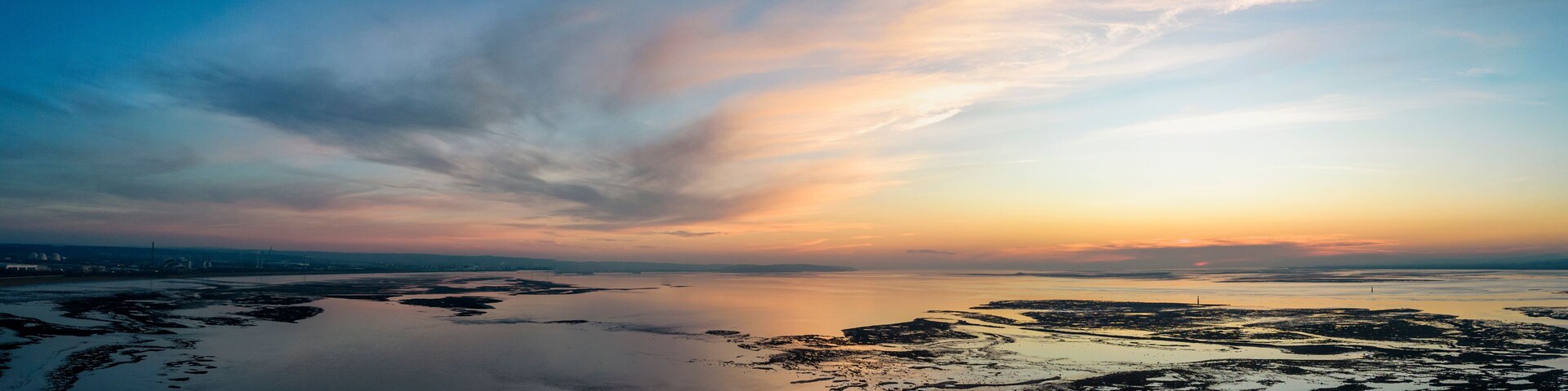 Un paisaje costero con mar en calma, cielo despejado y un atardecer.