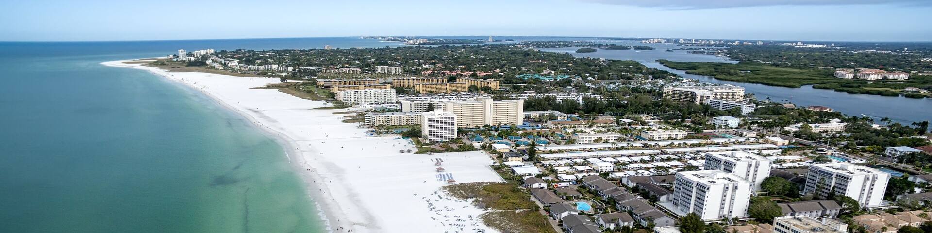 A coastal city with a long sandy beach, a marina, and several high-rise buildings.