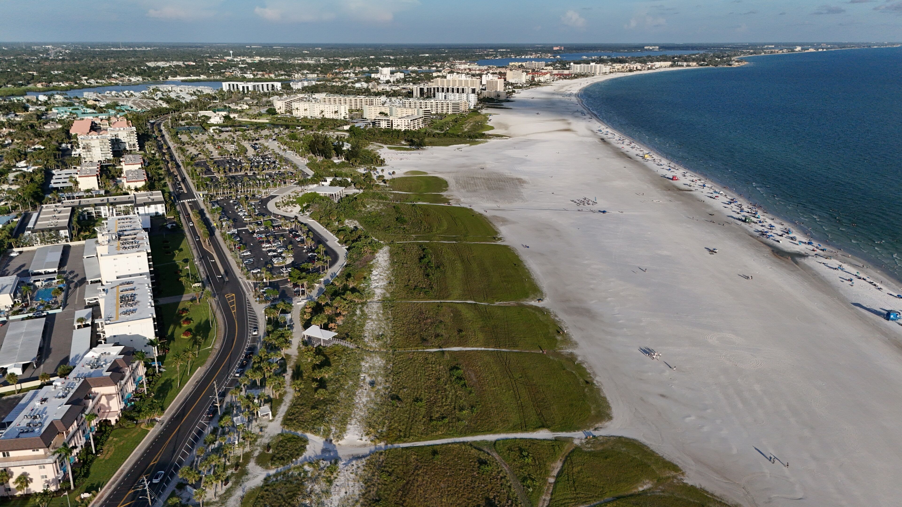 A coastal cityscape with a wide sandy beach, a marina, and high-rise buildings.